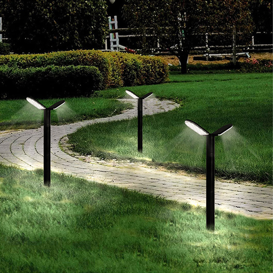 Curved stone pathway lit by black solar garden lights at dusk, with a green lawn, trimmed bushes, and a wooden fence near a playground in the background.