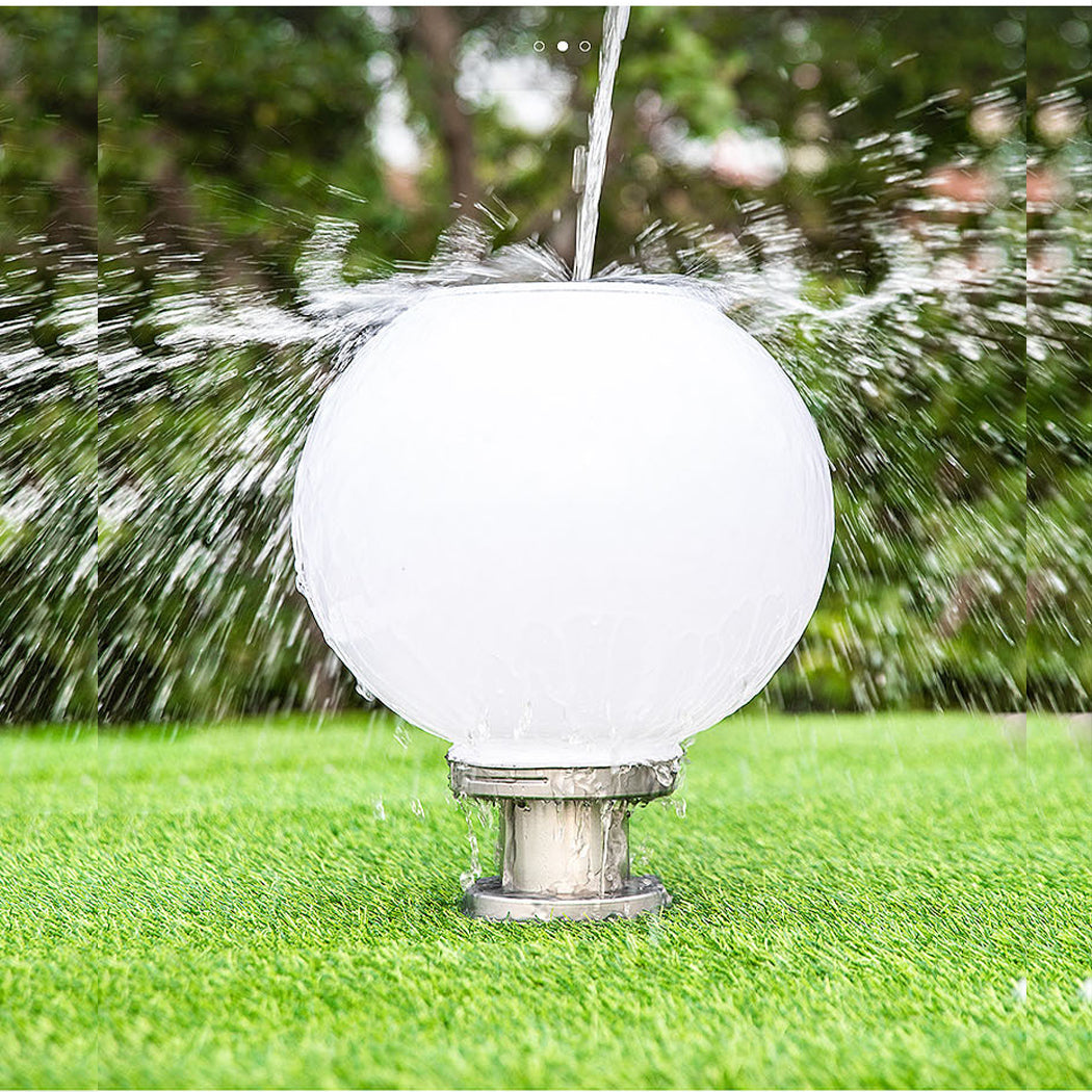 White solar garden globe light with stainless steel base, positioned on grass with water splashing against it to emphasize IP65 waterproof durability and outdoor resilience