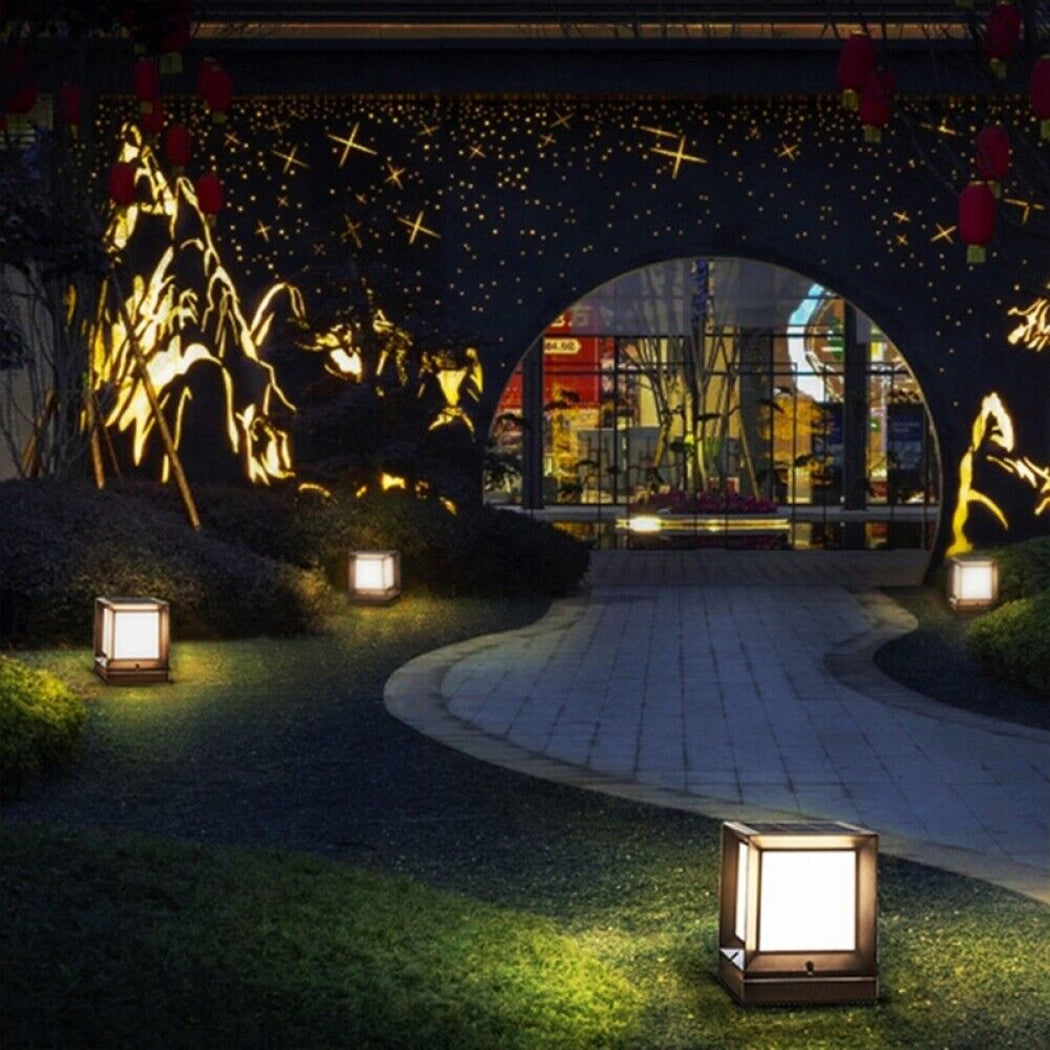 Square solar pillar lights illuminate a curved outdoor pathway in warm white mode, flanked by manicured grass and lush greenery. The sleek black fixtures feature top-mounted solar panels and sit atop stone pedestals, leading toward a decorative wall with glowing mountain and star motifs and an inviting arched entrance. Ideal for gardens, courtyards, or themed landscape designs that blend functionality with artistic flair.
Would you like a shortened version for mobile catalog use or something tuned for inter