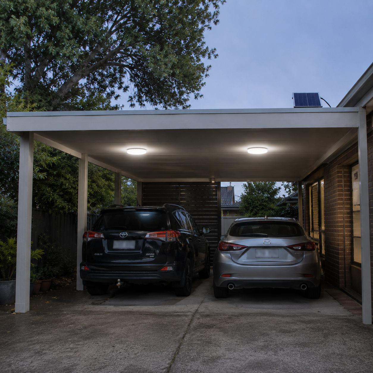 A double carport at twilight illuminated by two circle solar lights under the roof frame structure with a small solar panel mounted above to provide overhead security lighting for parked cars.