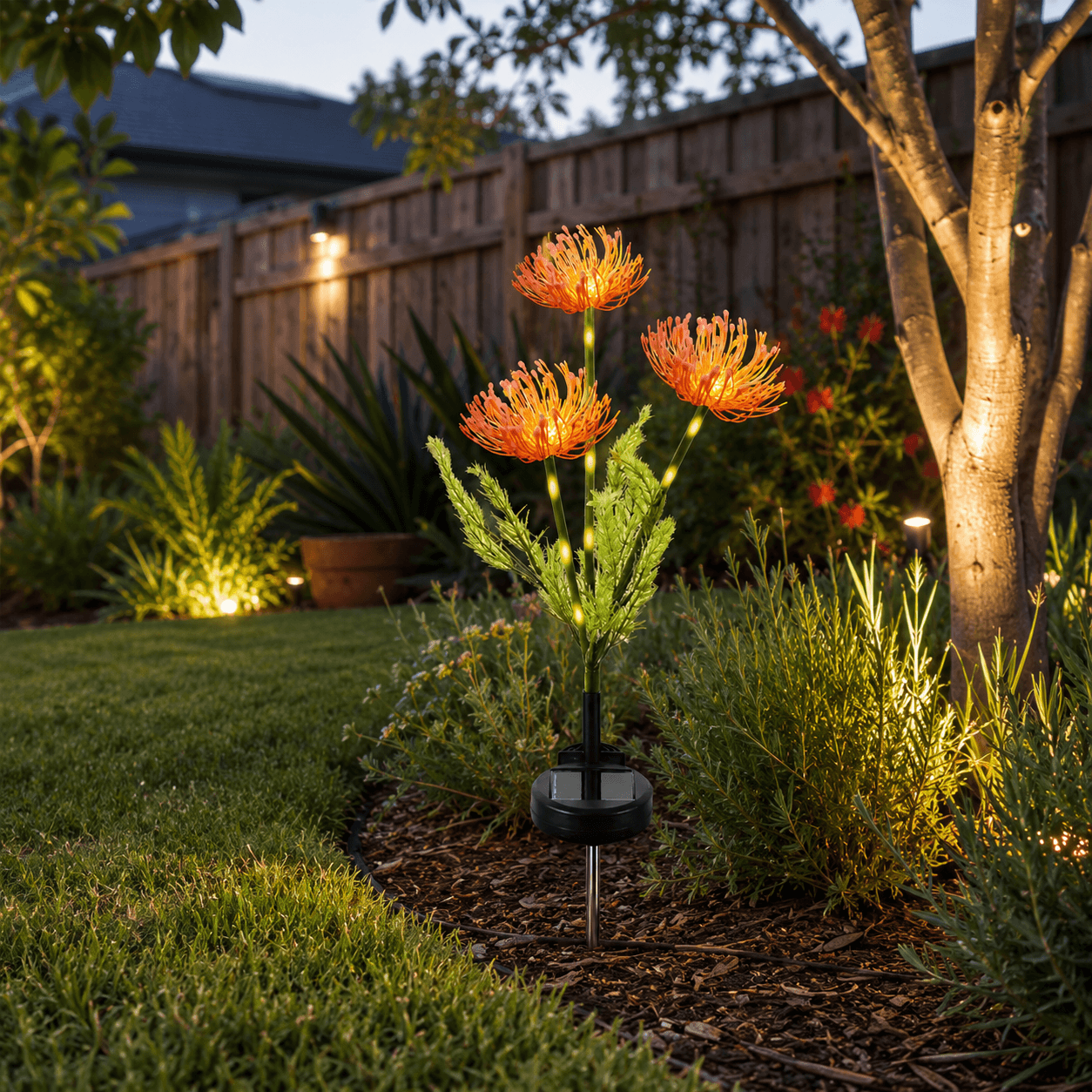 A three-headed orange spider lily solar garden stake light illuminating a backyard garden bed at dusk.