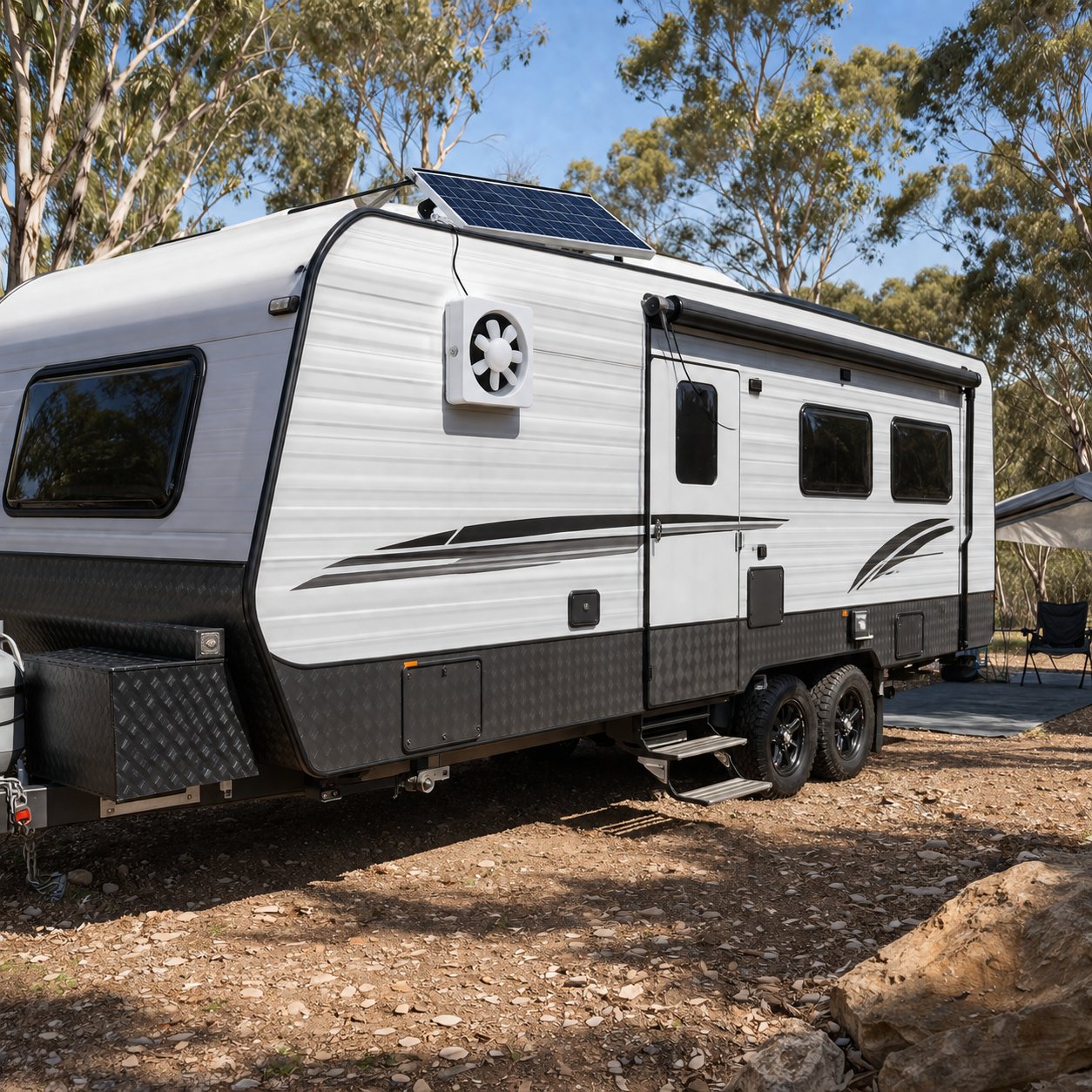 A solar powered ventilation fan installed on the side wall of a dual-axle caravan at an Australian campsite, with its roof-mounted solar panel providing off-grid air circulation and cooling.