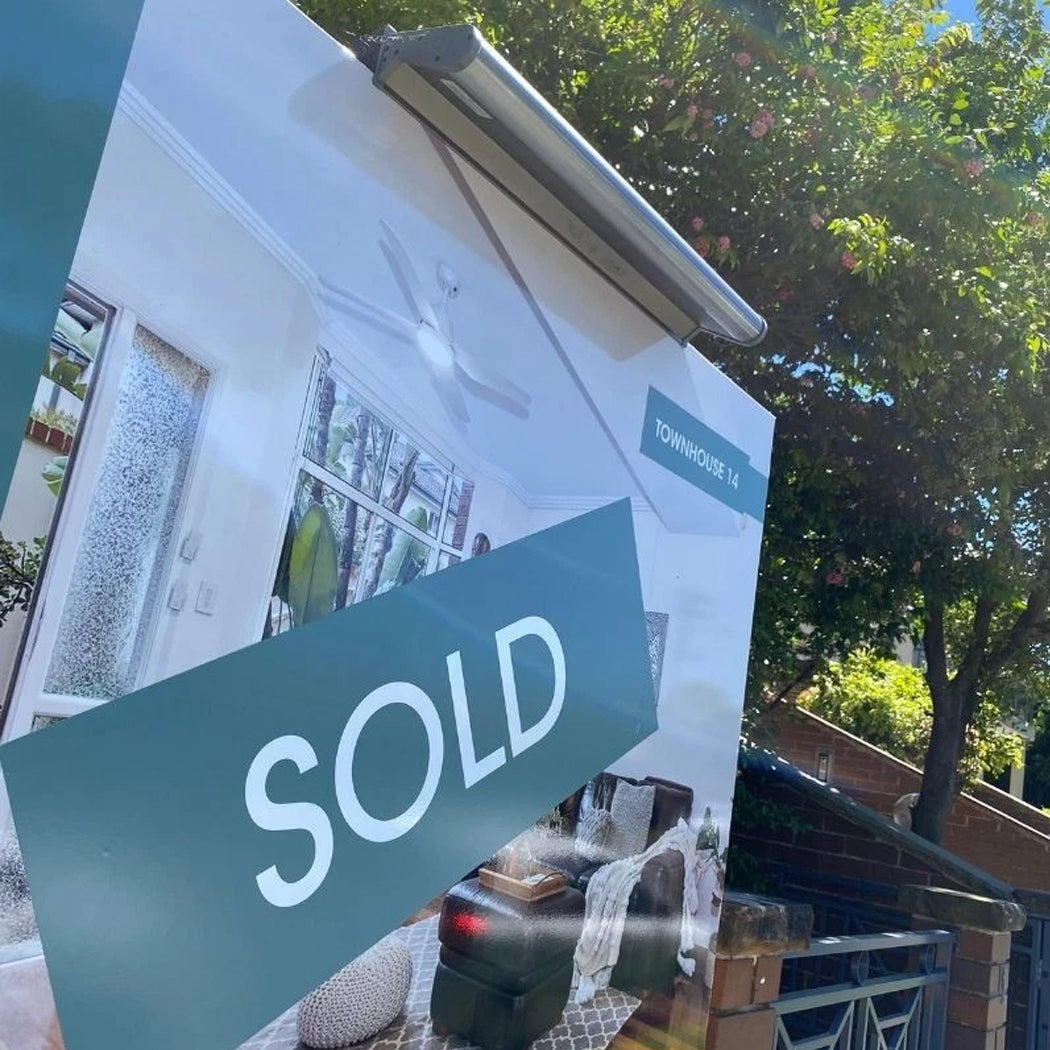 Real estate billboard displaying a 'SOLD' sign for Townhouse 14, illuminated by a solar-powered LED light mounted above. The fixture provides targeted lighting for the sign, enhancing visibility in outdoor settings. Its integrated solar panel and weather-resistant design make it ideal for energy-efficient property advertising