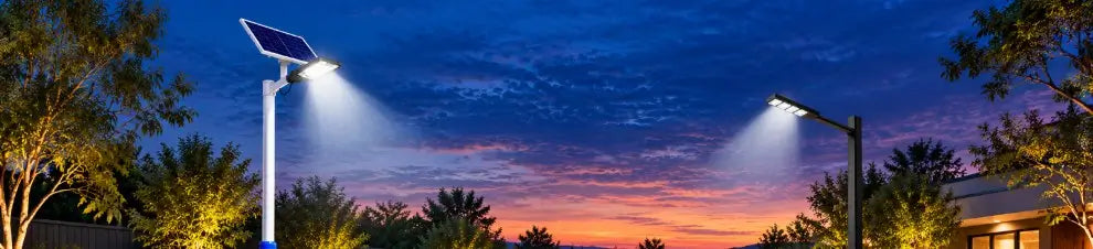 Two pole-mounted commercial solar street lights illuminating an outdoor driveway and residential property area against a vibrant sunset sky.