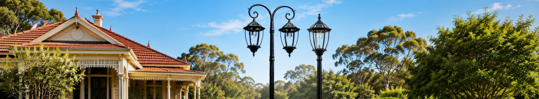 SolarEasy Victorian solar lamp posts including a double head coach lantern post light and a single head post light installed on the grounds of a classic Australian heritage home with a terracotta tile roof under a blue sky.