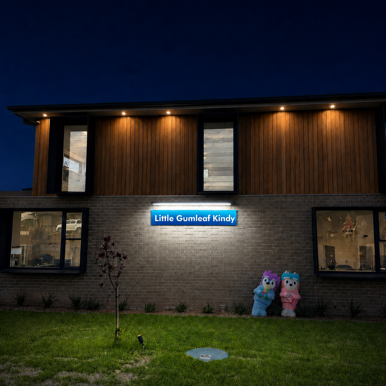 A 120cm outdoor solar sign lighting fixture illuminates a bright blue kindergarten business frontage panel mounted on a brick exterior wall at night.