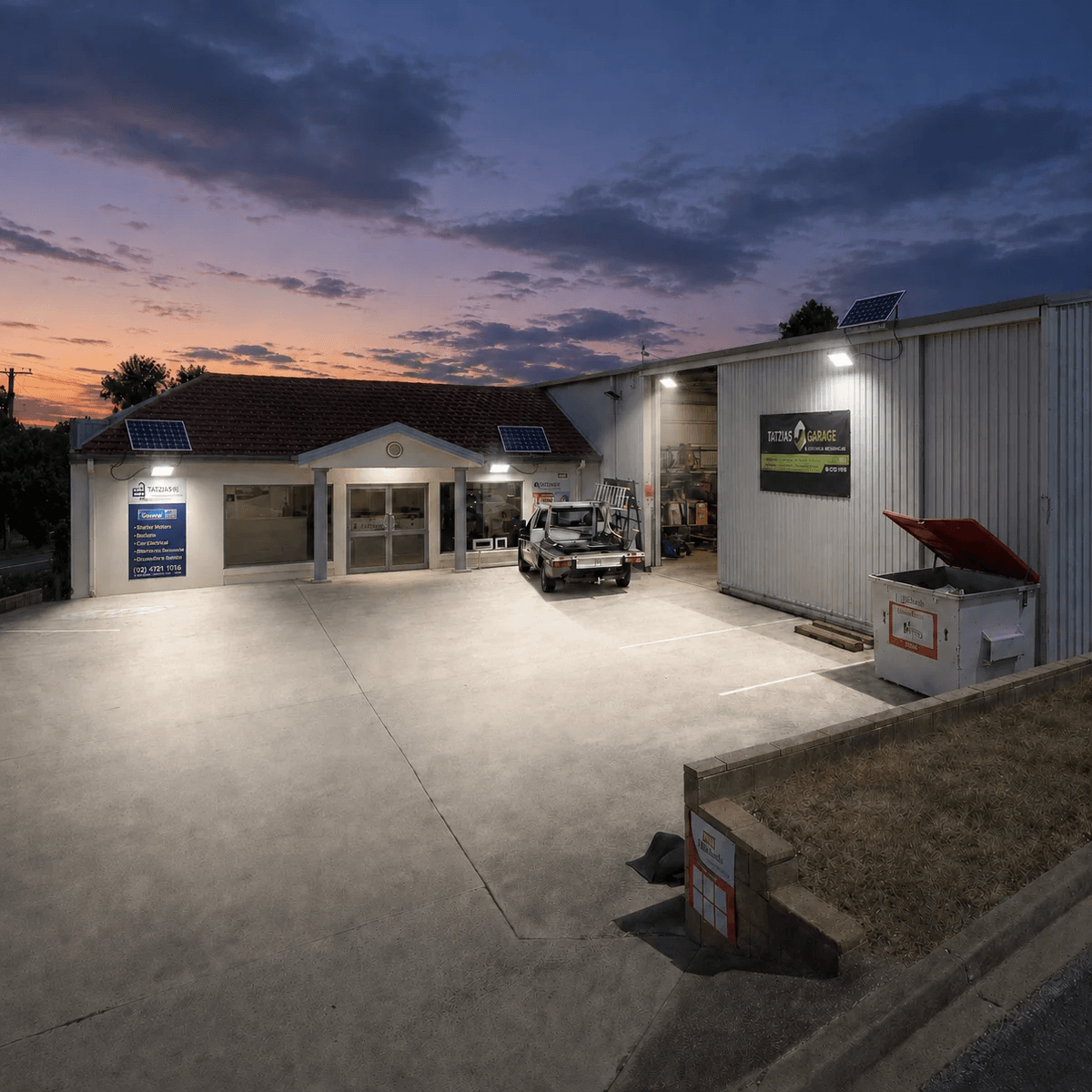 Commercial 300W floodlight solar powered units mounted on a mechanical garage workshop and concrete driveway forecourt for business outdoor security.