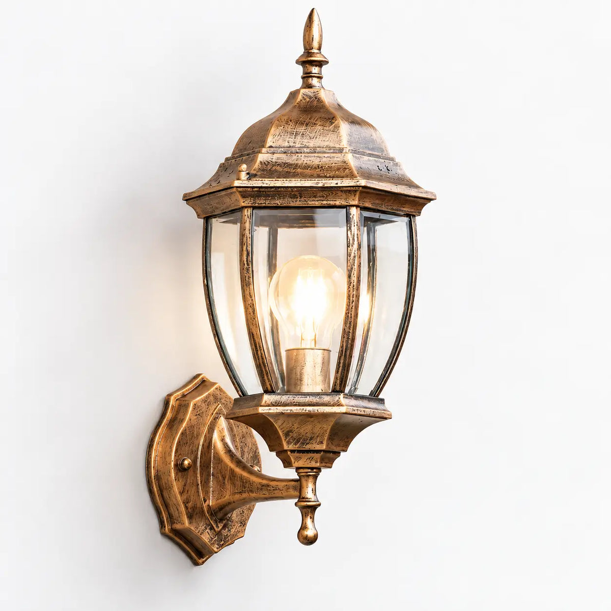 Side profile view of the antique bronze outdoor wall lantern showing the die-cast aluminium base plate mount, projecting bracket arm, and glowing warm white E27 bulb enclosed by clear glass panels.