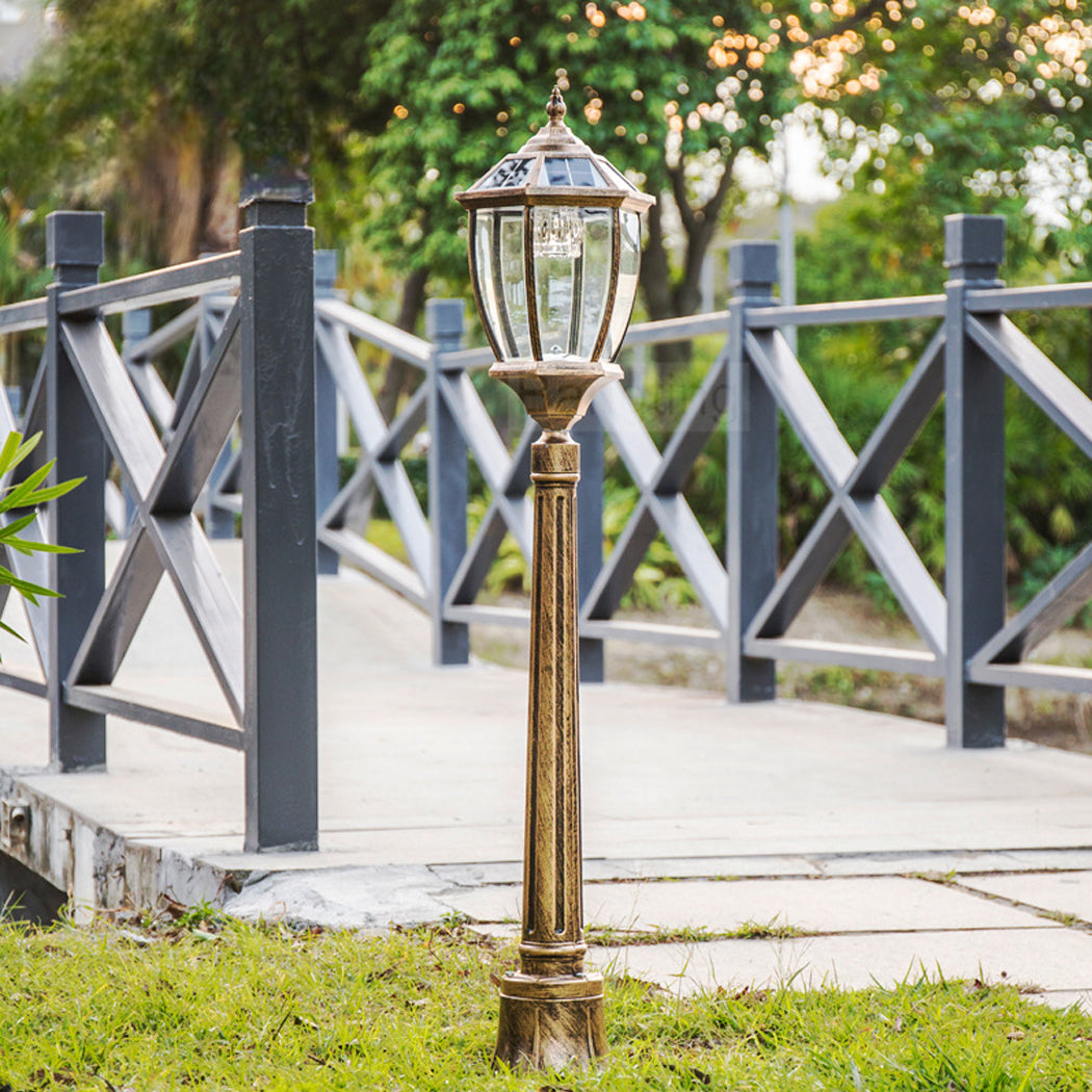 Antique bronze solar pathway post light with a clear glass lantern installed next to a garden walkway bridge.