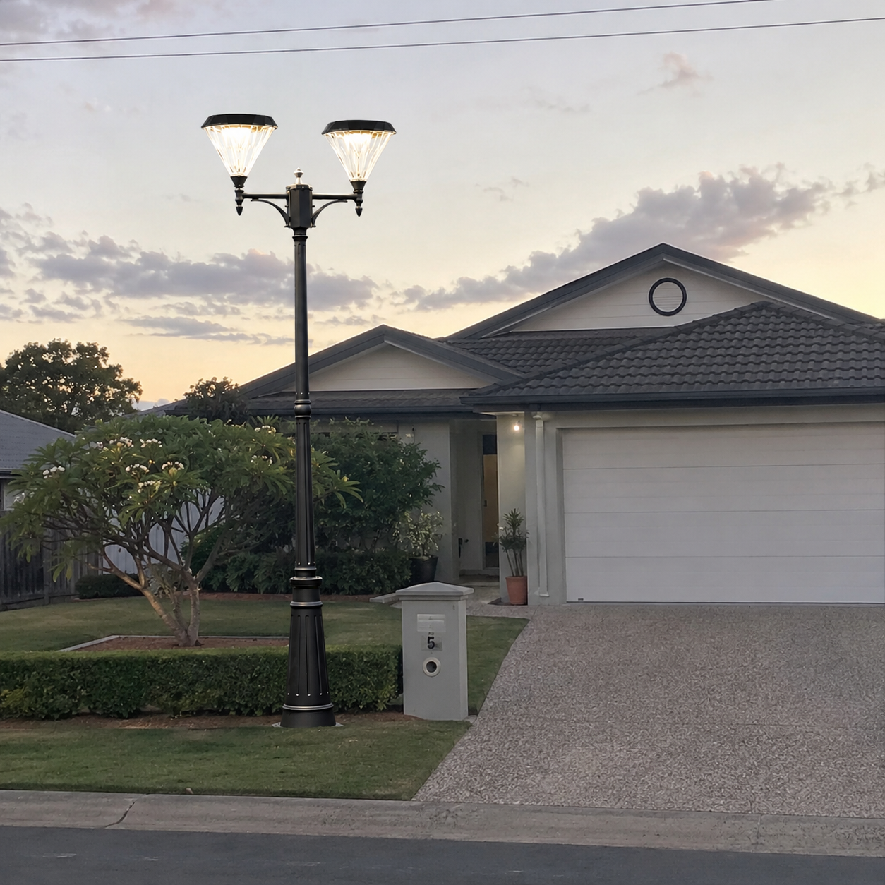 Flat top double head solar street light illuminated at dusk in front of an Australian home driveway and garden landscape.