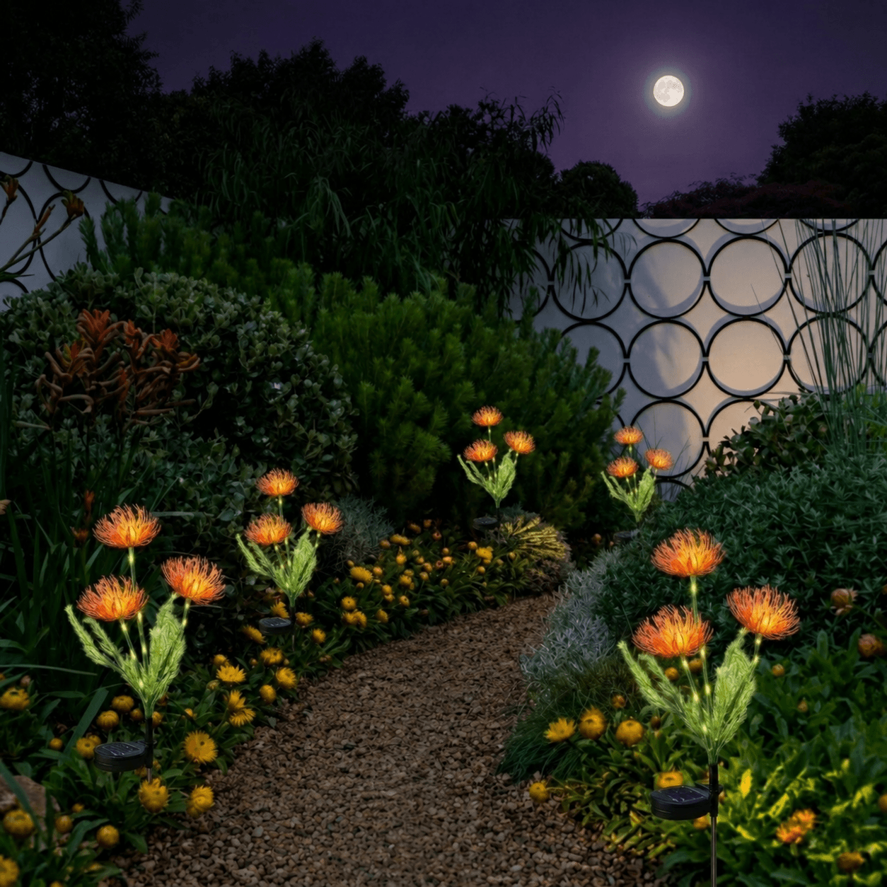 Multiple orange spider chrysanthemum solar stake lights flowers illuminating a winding gravel pathway in a landscaped backyard garden under a full moon.