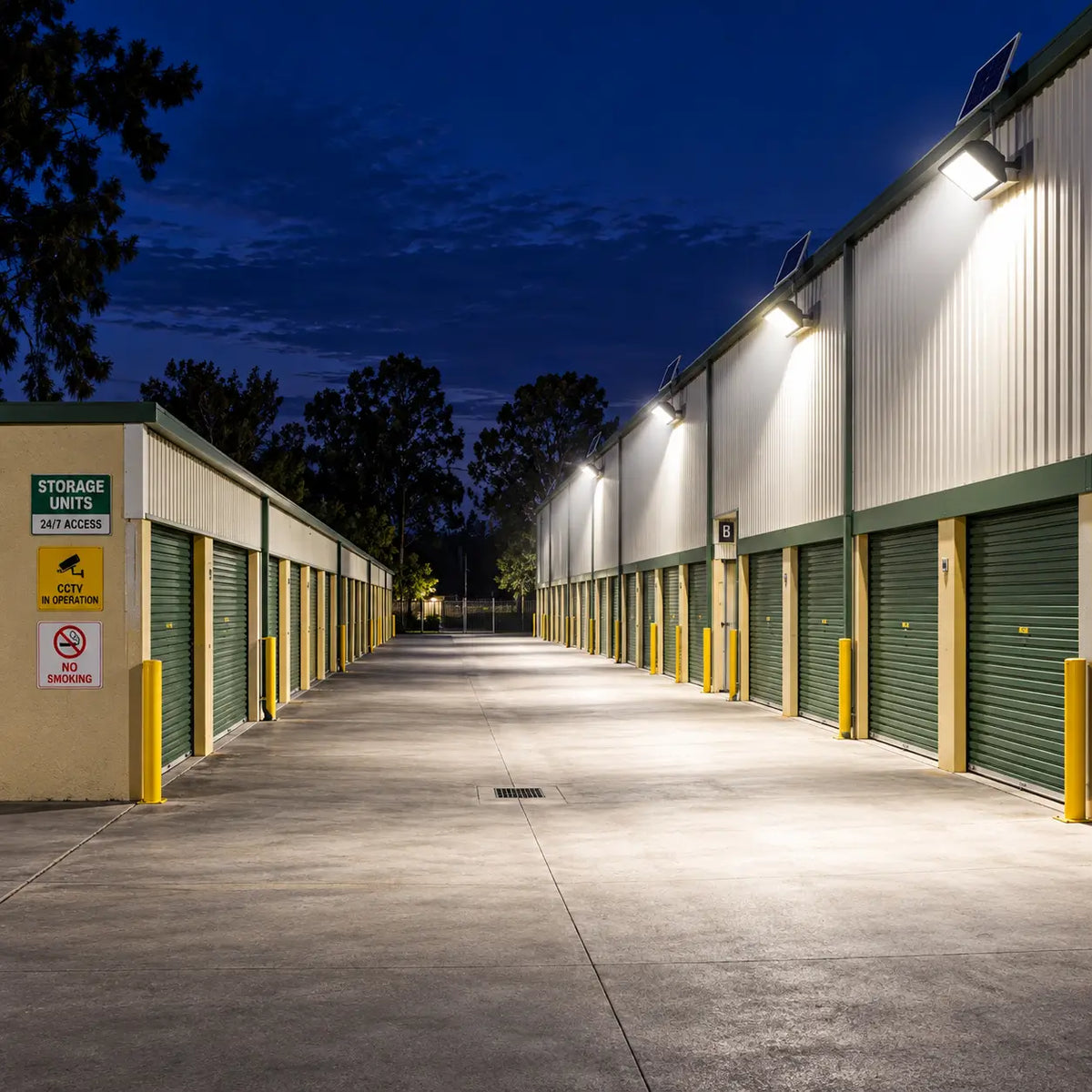 Multiple Rainman K90 commercial solar flood lights wall-mounted across a large self storage unit facility, casting bright 6,500 lumens security lighting over roller doors, concrete driveways, and security signage at night.