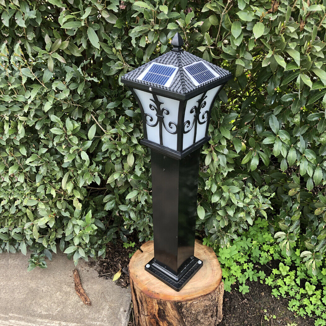 Solar pillar light black finish mounted on a wooden stump base next to garden hedges, showcasing a decorative outdoor installation setup.