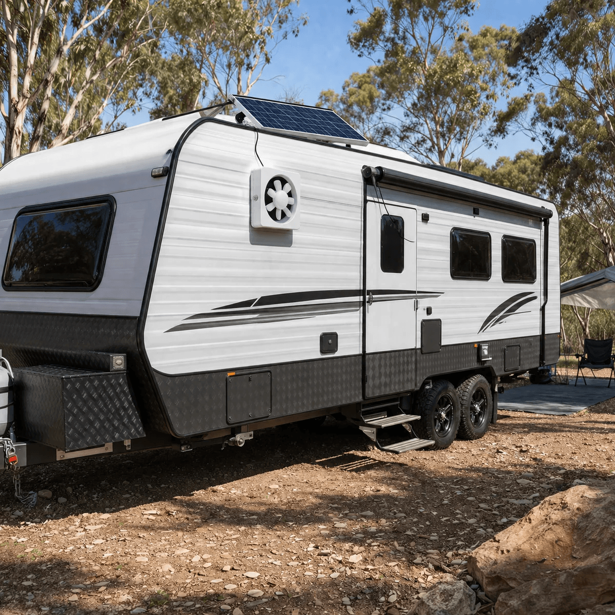 A solar powered ventilation fan installed on the side wall of a dual-axle caravan at an Australian campsite, with its roof-mounted solar panel providing off-grid air circulation and cooling.