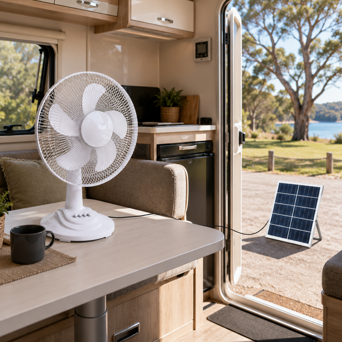 White solar powered table fan operating inside a caravan kitchen dining area, with its charging cable running out the open door to the solar panel sitting on the grass outside.